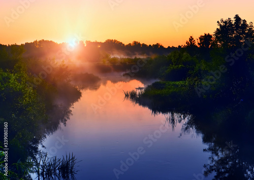 Fototapeta Naklejka Na Ścianę i Meble -  River in the early morning at dawn. Delicate dawn sky and fog rising above the water, lush greenery on the banks. Summer spring wild landscape by the river. Selective soft focus.