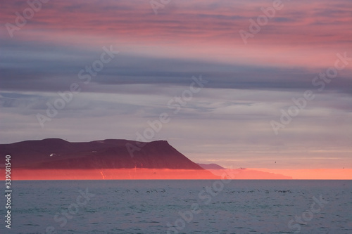 Amazing evening landscape of the coast of the Arctic Ocean with mountains  red fog and clouds at sunset. Beautiful summer nature of the Arctic. Chukchi Sea  Chukotka  Siberia  Far East of Russia.