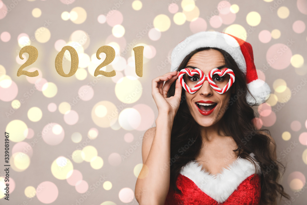 Emotional young woman in Christmas costume with party glasses on beige background. Bokeh effect