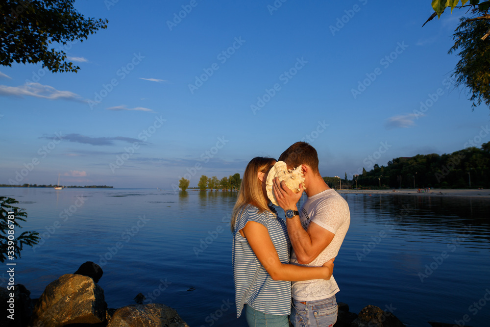 love story on the stone beach in evening. Young happy couple in love hugging and kissing on the beach in summer.
Romantic date in nature.
man and woman hold shell outdoors near river. 