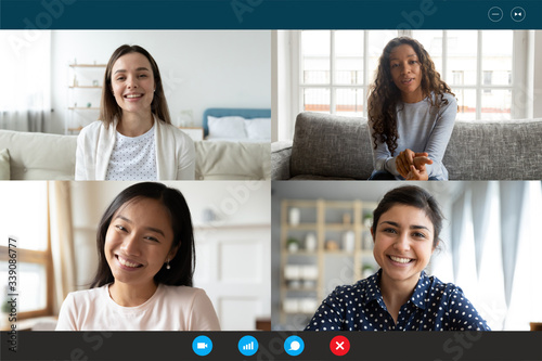 Laptop screen webcam view four multi ethnic beautiful millennial women involved in group video call. Meeting of friends on-line, colleagues working distantly, virtual communication modern tech concept photo