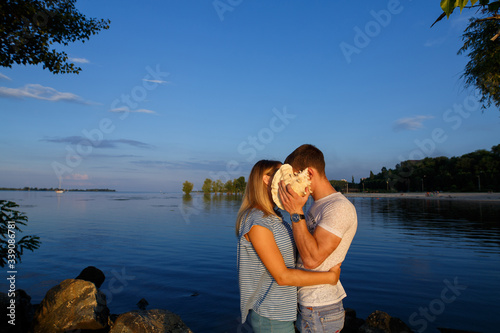 love story on the stone beach in evening. Young happy couple in love hugging and kissing on the beach in summer. Romantic date in nature. man and woman hold shell outdoors near river.  © mihail_pustovit