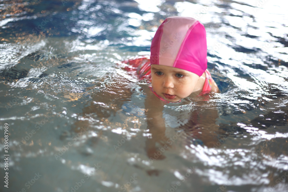 little girl in a pool cap and pink swimsuit learns to swim in the pool