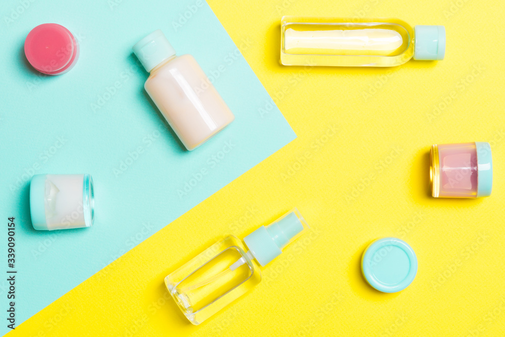 Top view of cosmetic containers, sprays, jars and bottles on yellow and blue background. Close-up view with empty space for your design Top view of cosmetic containers, sprays, jars and bottles on yellow and blue background. Close-up view with empty space for your design