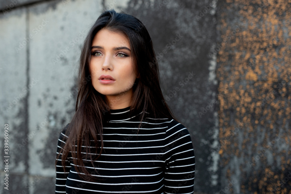 Profile of a young beautiful girl with straight brunette hair, looking away, with makeup, near the black wall. Horizontal view.