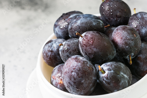 Plum in a white ceramic bowl on a light gray table. Space for text. Seasonal fruits