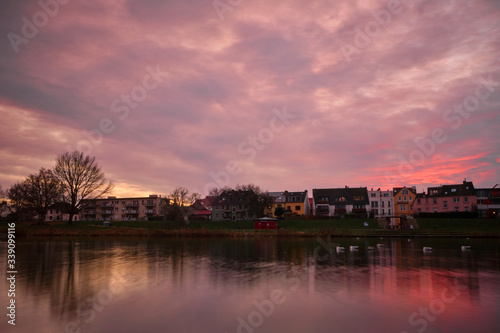 Epic sunset light casts over a calm German Lake with traditional houses in the background and birds on the water