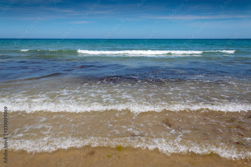 Waves rolling onto a sandy beach on a hot summer day with a blue sky and light clouds