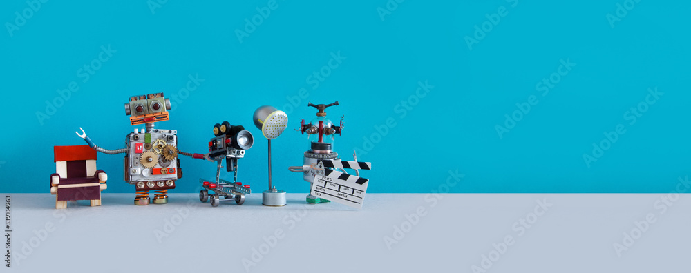 Robotic filmmaking backstage concept. Two robots shoots motion picture television episode or movie. Funny filmmakers director cameraman, cyborg assistant clapperboard on blue background, copy space