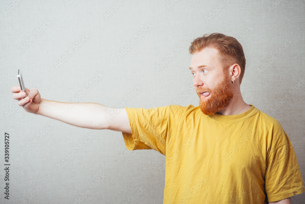on a gray background man with a beard in a yellow T-shirt photo of yourself on your mobile phone on a gray background man with a beard in a yellow T-shirt photo of yourself on your mobile phone