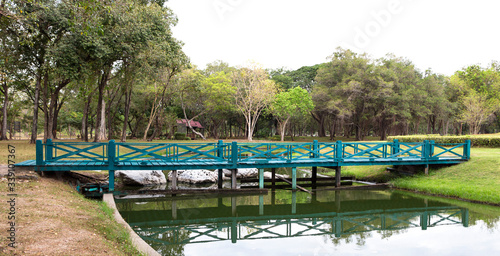 Fototapeta Naklejka Na Ścianę i Meble -  Old green wooden bridge in a peaceful and beautiful garden in tropical.