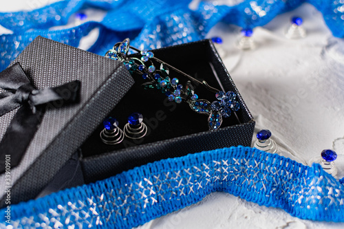 Beautiful brooch with blue and aquamarine stones and rhinestones of different sizes, metal base pins in a gift box with a black bow, around the ribbon with silver threads and springs.