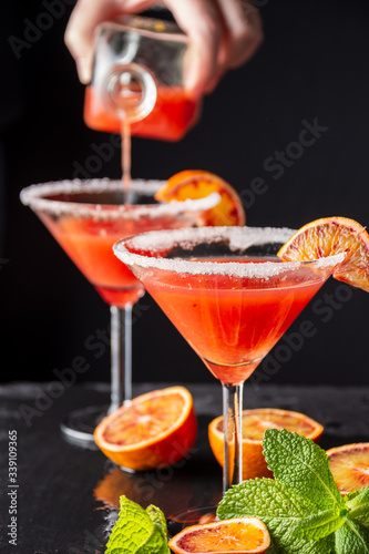 Top view of blood orange cocktail glasses with woman's hand serving, selective focus, and black background, vertical