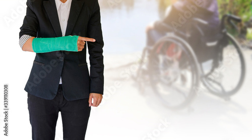 broken arm, injury woman standing wearing black suit isolated on blurred background patient sitting on wheelchair