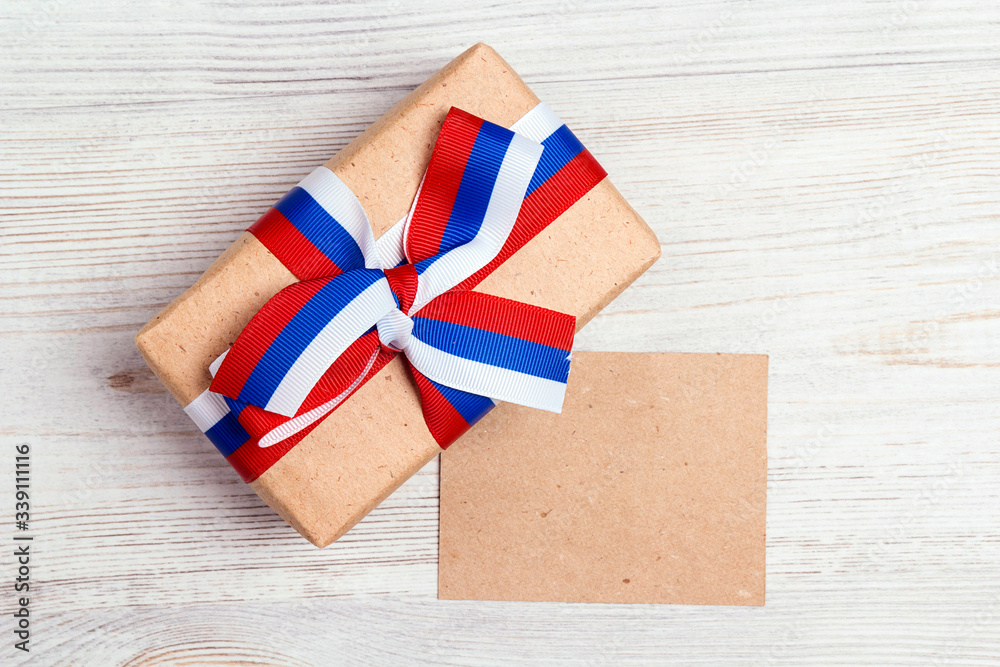 Fototapeta premium Gift box with Russian flag color ribbon on light wooden background and blank paper card.