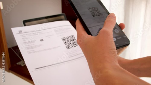 Hand with phone scans QR Code on background of a laptop with a workplace