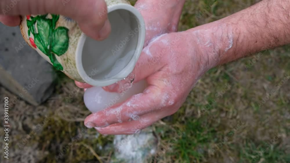 Man washes his hands with soap on a background of green grass. Water is poured from a ceramic pot. Man washes his hands with soap on a background of green grass. Water is poured from a ceramic pot.