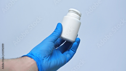 A male hand in a blue medical glove offers quarantine pills against coronavirus. Isolated on a gray background in the studio. Coronavirus concept. Stay at home.