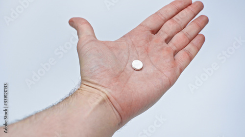 A male hand holds and shows a pill for treating coronavirus during quarantine. Isolated on a gray background in the studio. Coronavirus concept