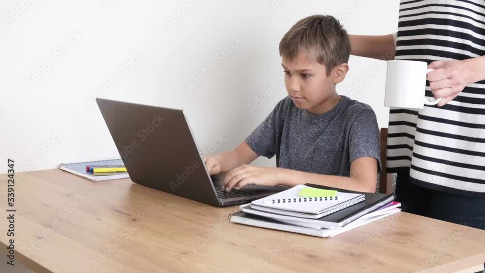Child learning with laptop computer, doing homework at home. Mother come to support him. Technology, distance education, online learning from home Child learning with laptop computer, doing homework at home. Mother come to support him. Technology, distance education, online learning from home