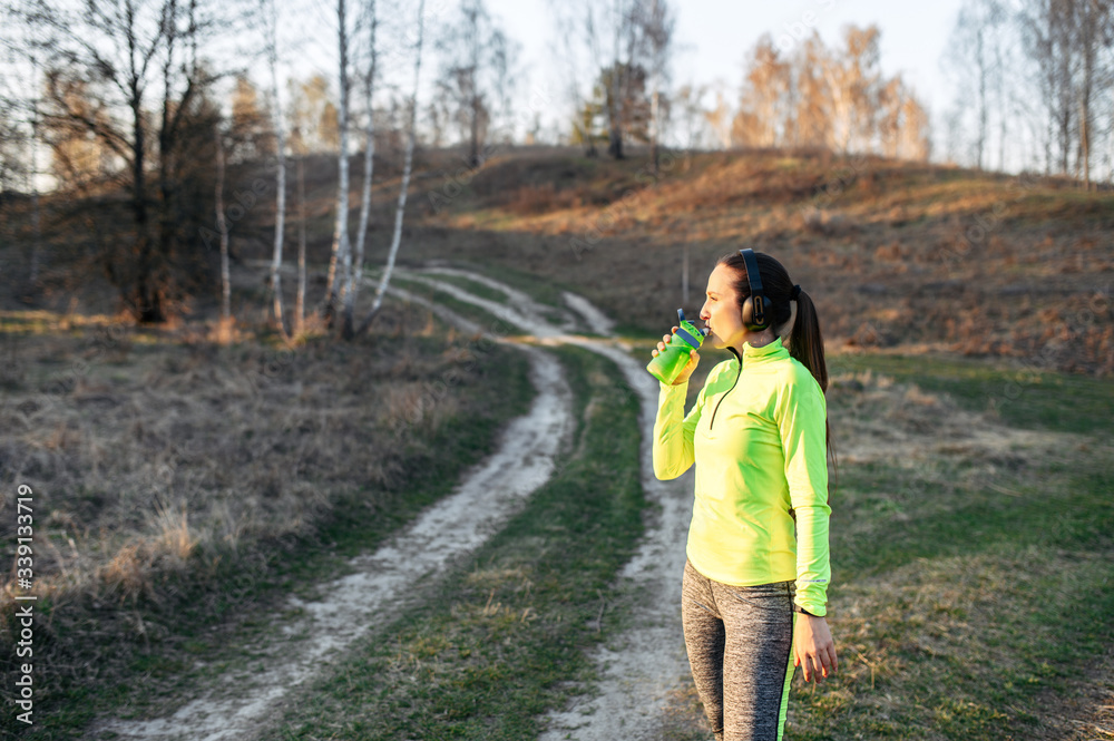 Fototapeta premium Young woman in sportswear outdoors drinks water
