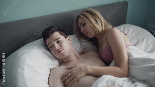Worried thoughtful woman sitting on bed feels sad and troubled, pensive wife looking at sleeping husband frustrated by sexual problems, difficulties in relationships, thinking of breaking up divorce