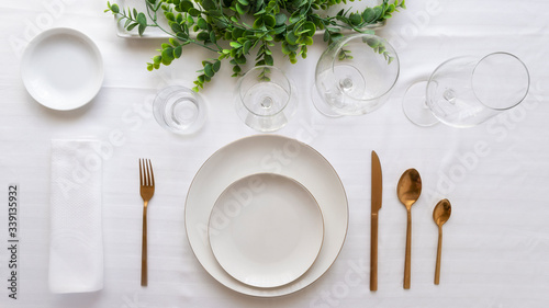 Table setting for elegant festive dinner with white porcelain plates, glasses, decorative textile gold cutlery and center place.