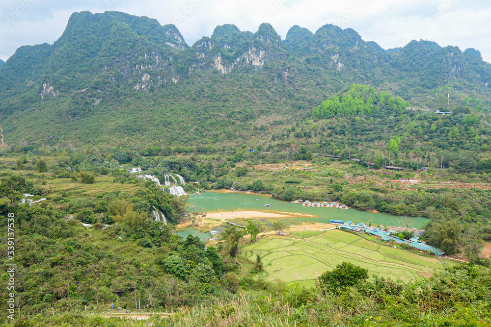 Fototapeta premium Full of water huge waterfall near the green forest with green trees in mountains from the top view.