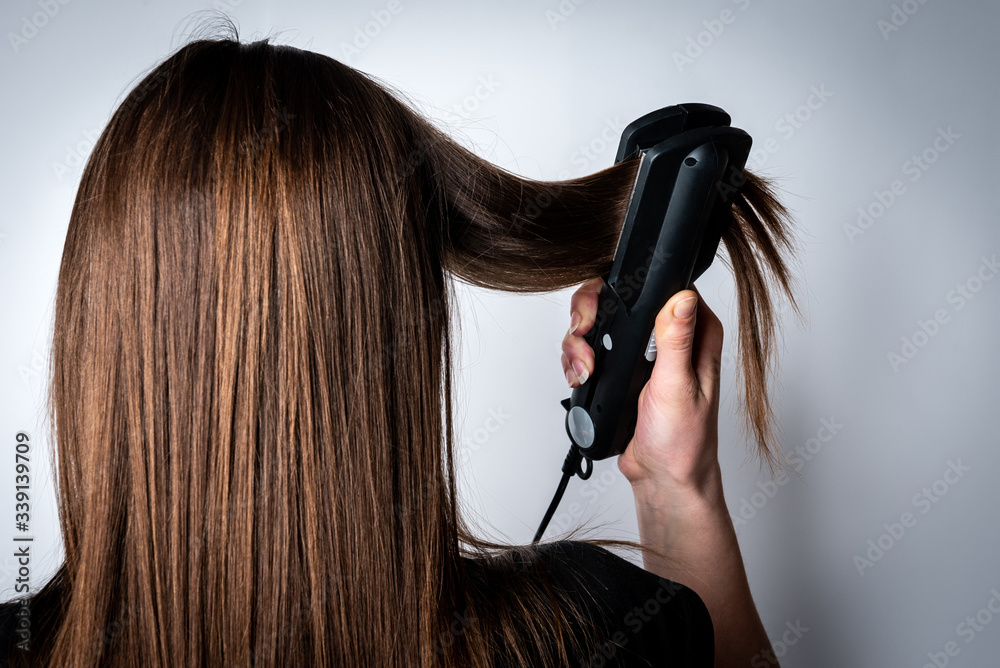 Fototapeta premium Young woman straightens her hair on gray background.