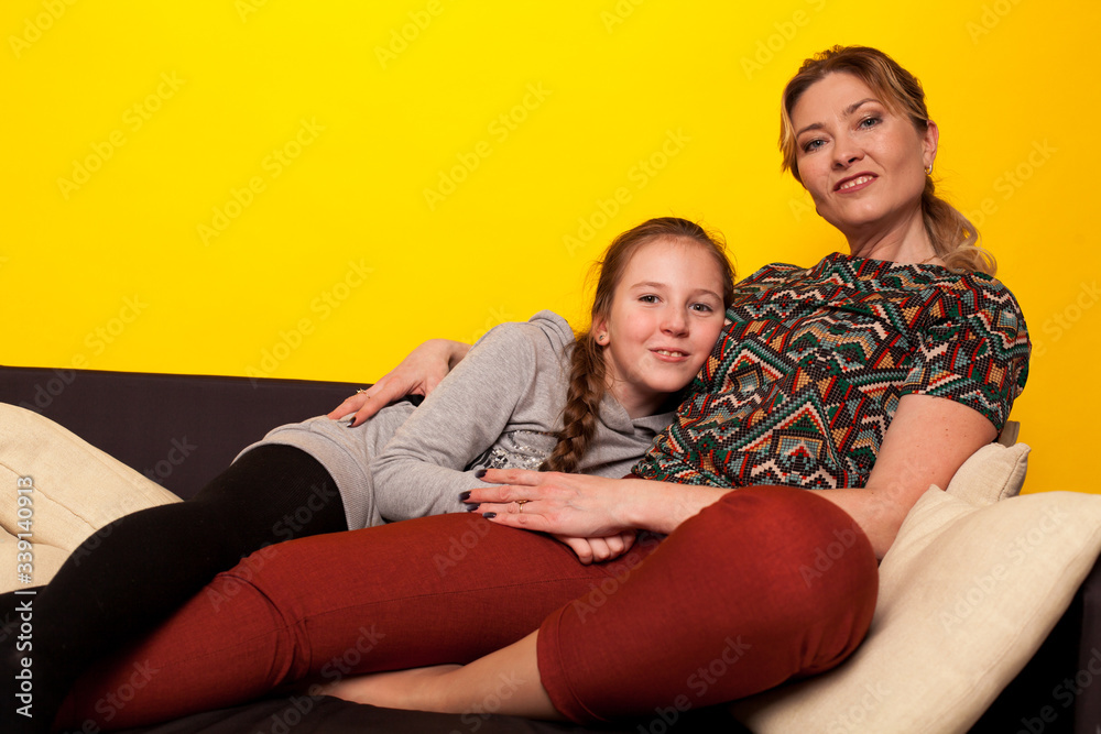 Mom and daughter sit at home in a room on the family couch Mom and daughter sit at home in a room on the family couch