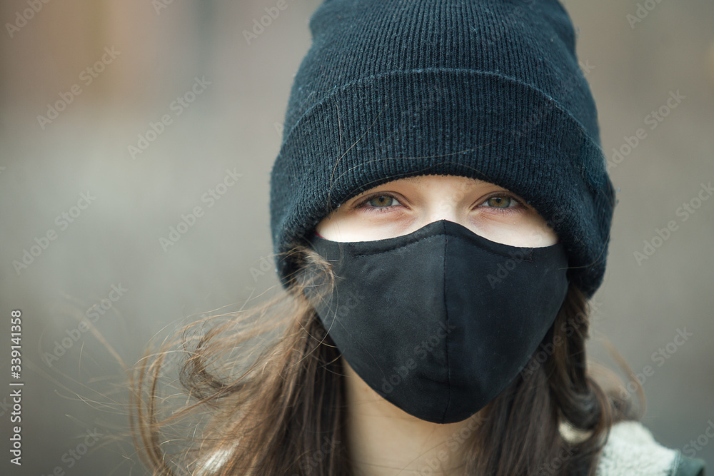 Portrait of a young girl in the ear loop mask and black cap, close up. Teenager in facial mask