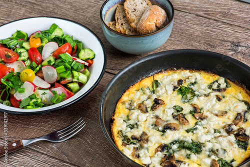 Homemade omlette with cheese, 
mushrooms and spinach in pan on wooden table. Homemade Frittata.