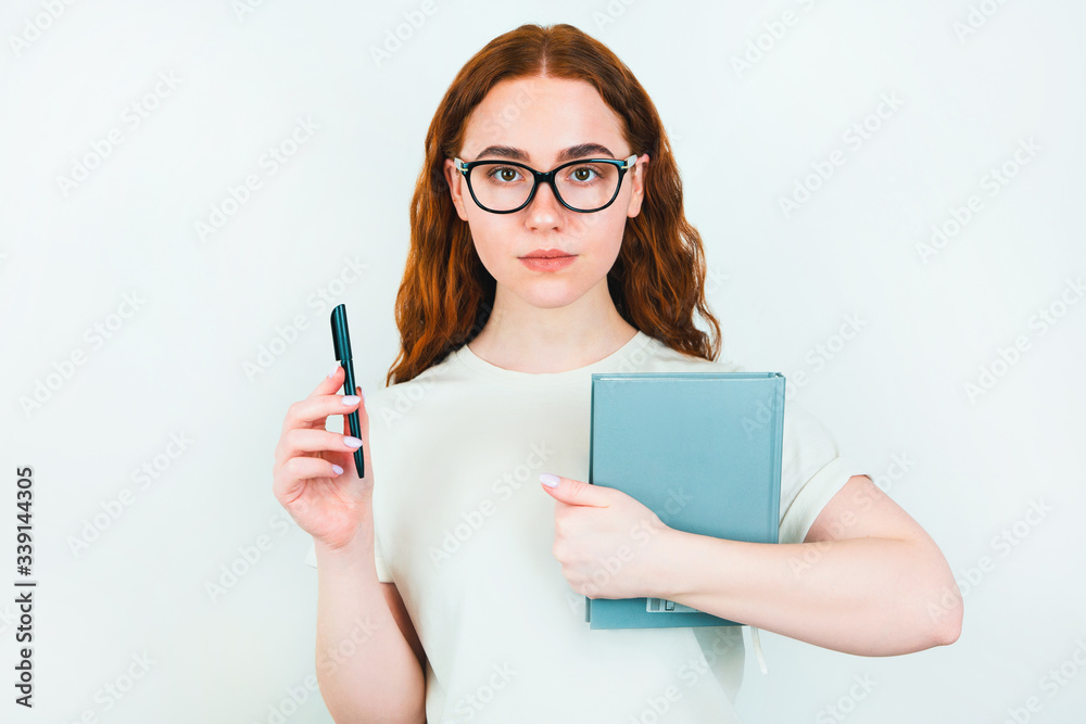 redheaded serious woman in eyeglasses holding pen in one hand and planner in another standing on isolated white backgroung, learning and teaching concept redheaded serious woman in eyeglasses holding pen in one hand and planner in another standing on isolated white backgroung, learning and teaching concept