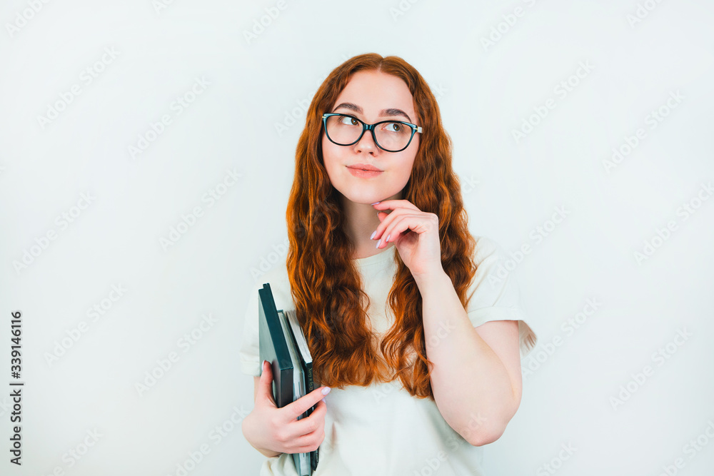 redheaded woman student in eyeglasses with books in her hand looks thoughtful standing on isolated white backgroung, learning and teaching concept redheaded woman student in eyeglasses with books in her hand looks thoughtful standing on isolated white backgroung, learning and teaching concept