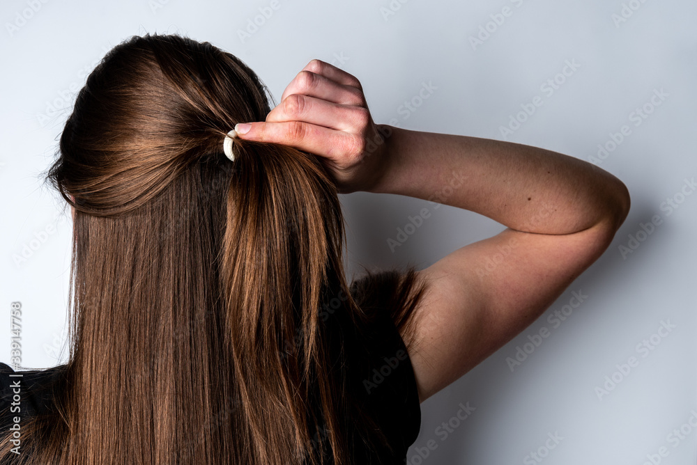 Woman collecting hair in a ponytail on gray background. Woman collecting hair in a ponytail on gray background.