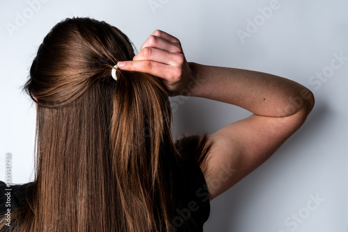 Woman collecting hair in a ponytail on gray background.