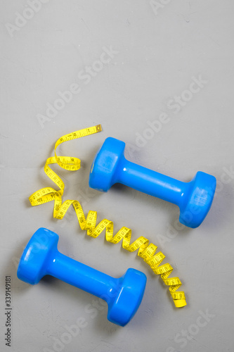 dumbbell and centimeter on a light background