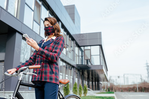 businesswoman in plaid mask using smartphone near bicycle outside © LIGHTFIELD STUDIOS
