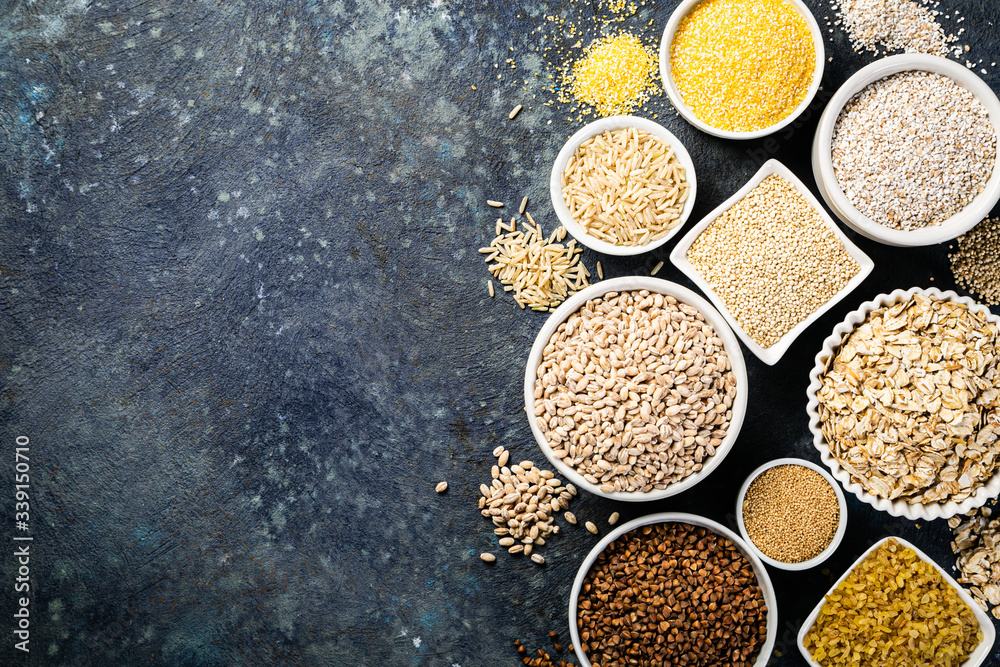 Selection of whole grains in white bowls - rice, oats, buckwheat, bulgur, porridge, barley, quinoa, amaranth on dark background