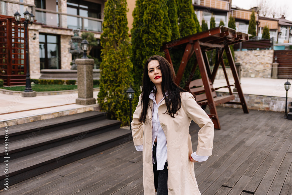 Young beautiful woman in beige coat with a bag walking on the autumn street