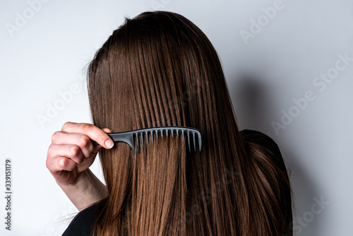 Young woman combing her hair on gray background.