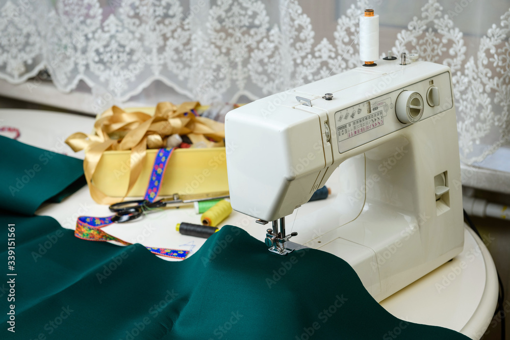 Sewing machine on the table, green cloth in the foreground. Concept - sewing as a hobby.