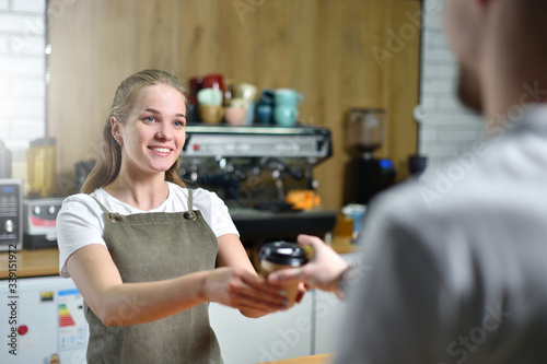 A young barista girl sells takeaway coffee and hands it to a client. Small business concept