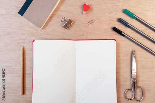 Blank open notebook with office supplies: scissors, pencils, pens and clips. Flat lay, top view