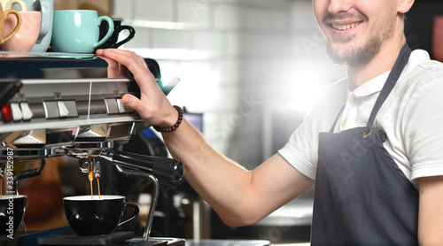 A young barista guy makes coffee on a large professional coffee machine. Small business and work concept for young people