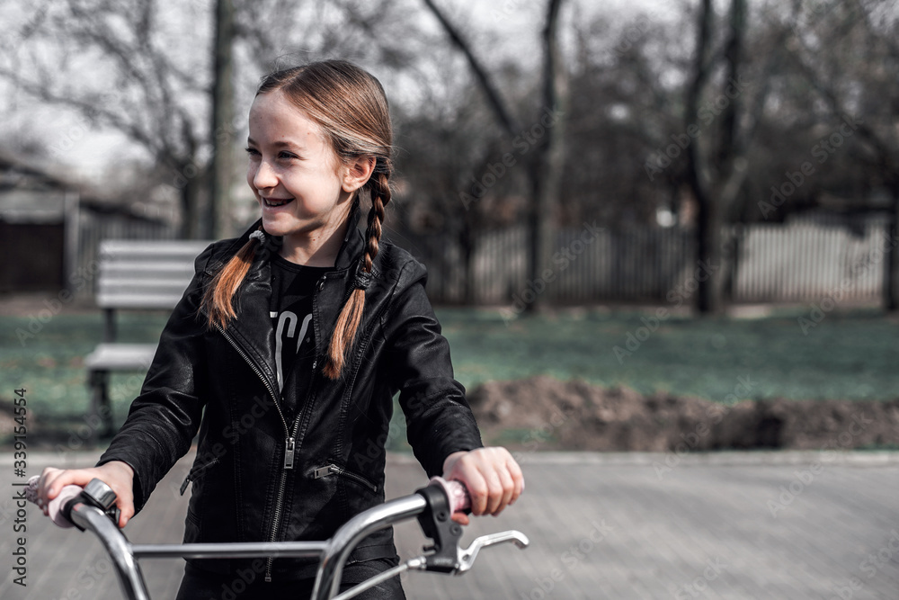 Girl on a bike ride. Portrait of a girl with braids in a leather jacket on a bicycle. The girl is joyful and smiling. Sports activity