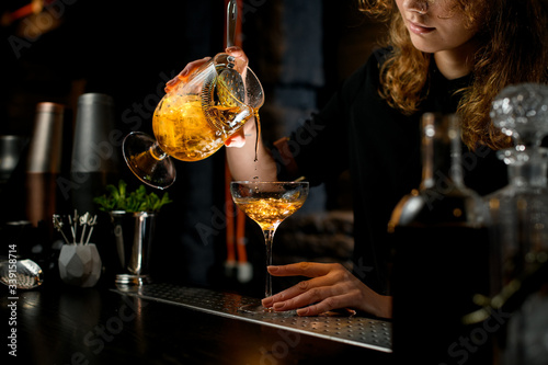 Close-up. Young pretty barman pours ready-made cocktail into glass. photo