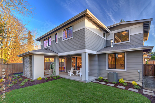 Large modern grey new house with back porch from back yard with green grass and nice landscaping.