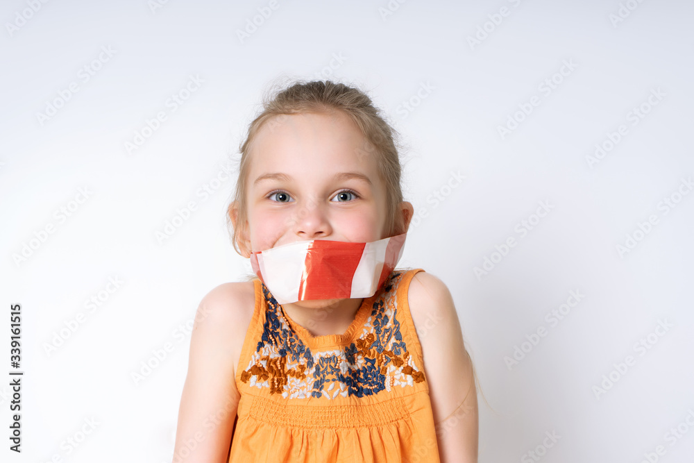 Blond little model in orange blouse posing isolated on white. Her mouth is tied with a white and red warning tape. Quarantine. restriction of freedom, stay at home. Close copy space Blond little model in orange blouse posing isolated on white. Her mouth is tied with a white and red warning tape. Quarantine. restriction of freedom, stay at home. Close copy space