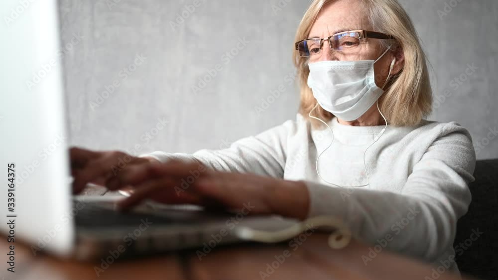 Technology, old age and people concept - lonely sad older senior woman in face medical mask working and making a video call with laptop computer at home during coronavirus COVID19 pandemic. Stay home Technology, old age and people concept - lonely sad older senior woman in face medical mask working and making a video call with laptop computer at home during coronavirus COVID19 pandemic. Stay home